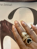 White and black heart rings with a clear-stone crown ring worn together on a hand.